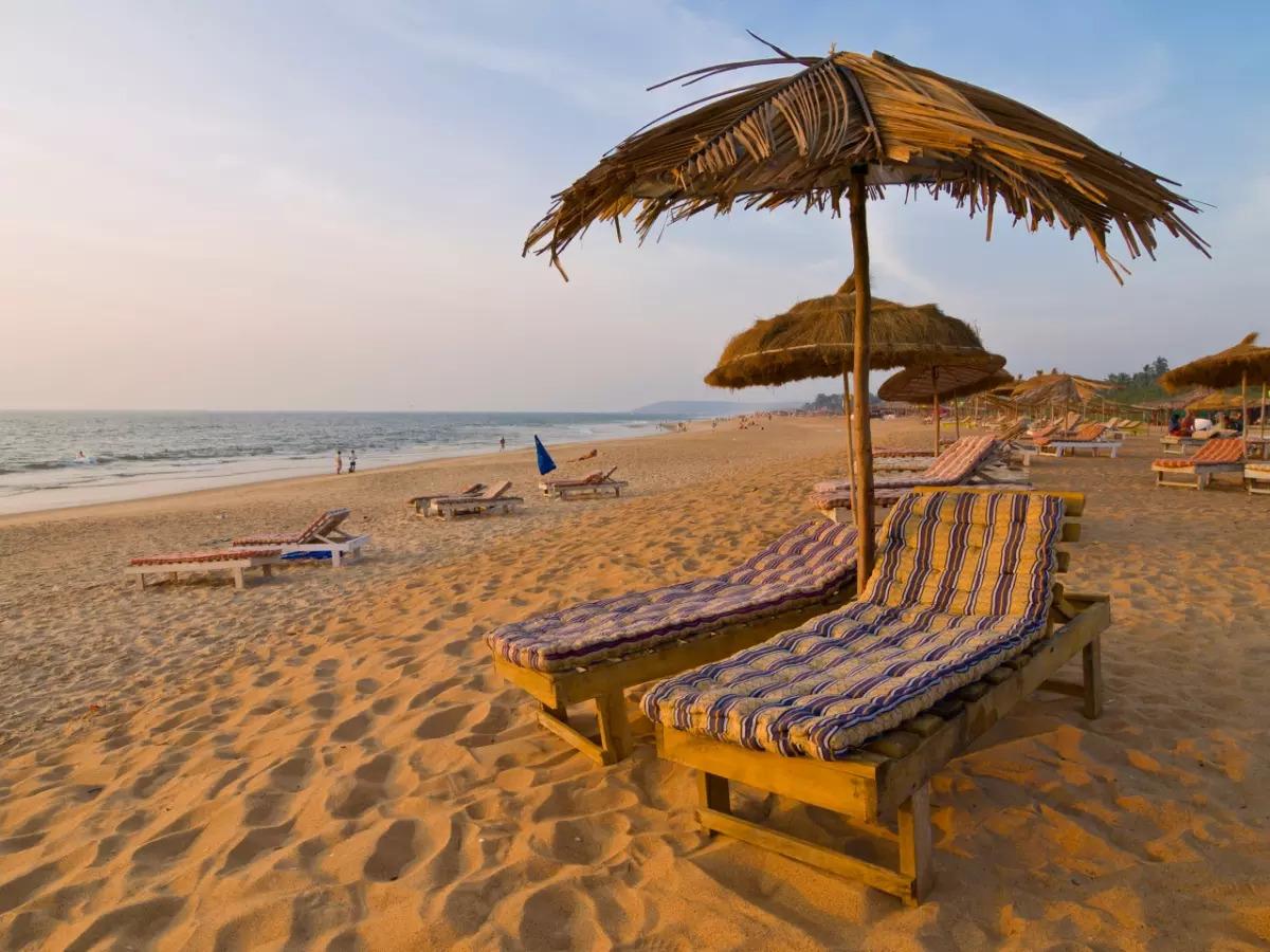 People enjoying a relaxing day at Calangute Beach in North Goa with golden sand, clear blue waters, palm trees, and a scenic coastal backdrop.